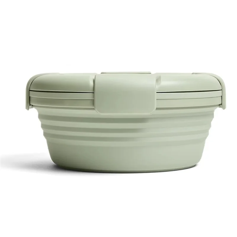 Green collapsible food container on a wooden surface with a mug and bottle in the background.