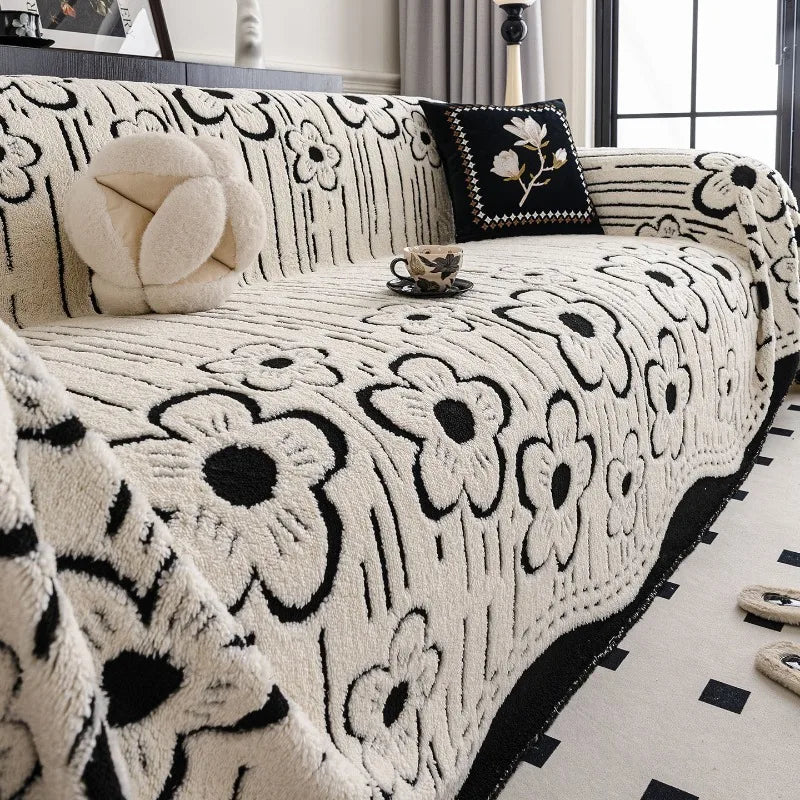 Cream and black floral-patterned sofa throw with bold contrast edging, neatly layered over a modern armchair sofa in a bright interior setting.