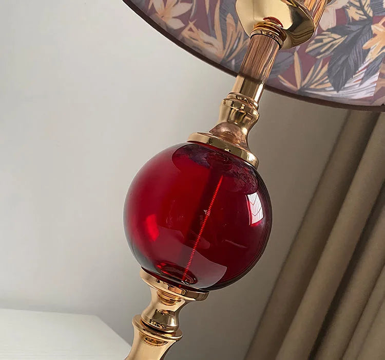 Close-up of a lamp with a red glass globe and gold fixture.