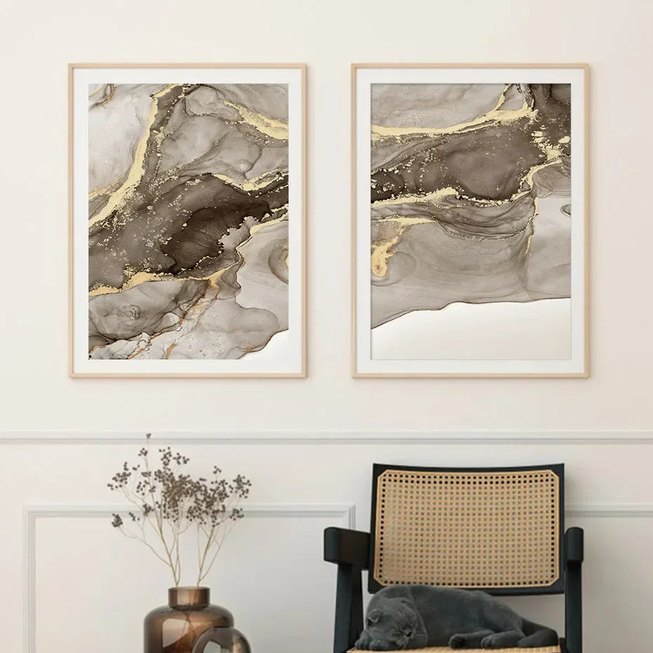 Two abstract art pieces in gold and gray frames on a wall above a chair with a cat.