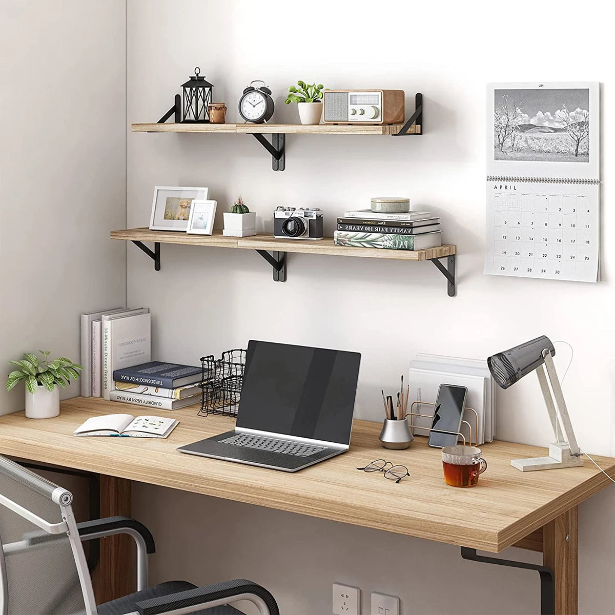 Home office setup with a wooden desk, laptop, lamp, and shelves on a white wall.