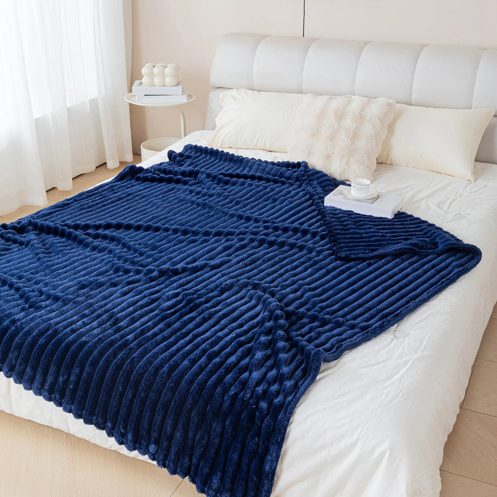 Blue textured blanket draped over a white bed in a bedroom setting.