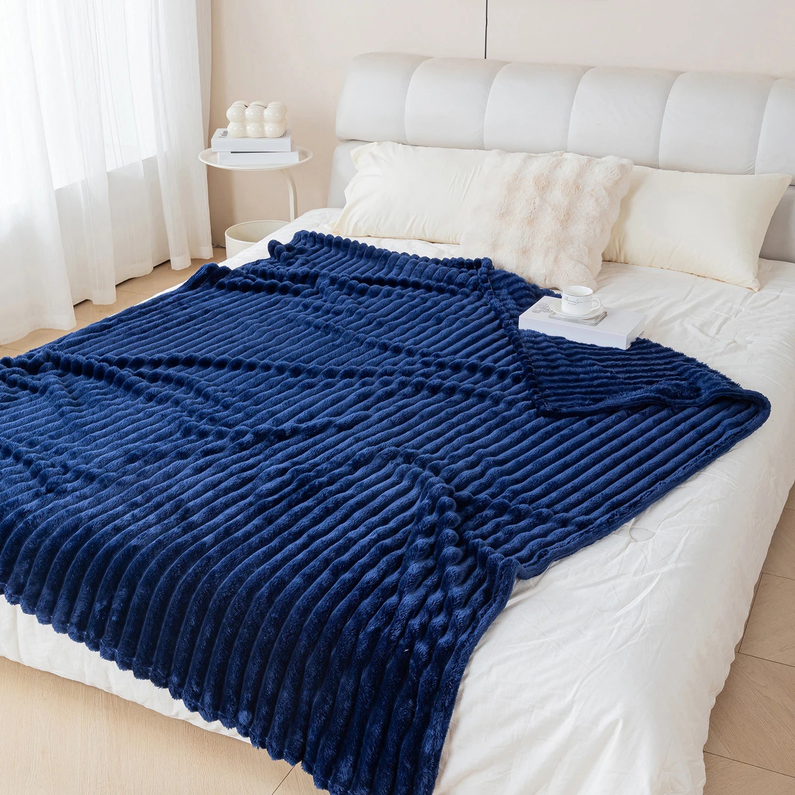 Blue textured blanket draped over a white bed in a bedroom setting.