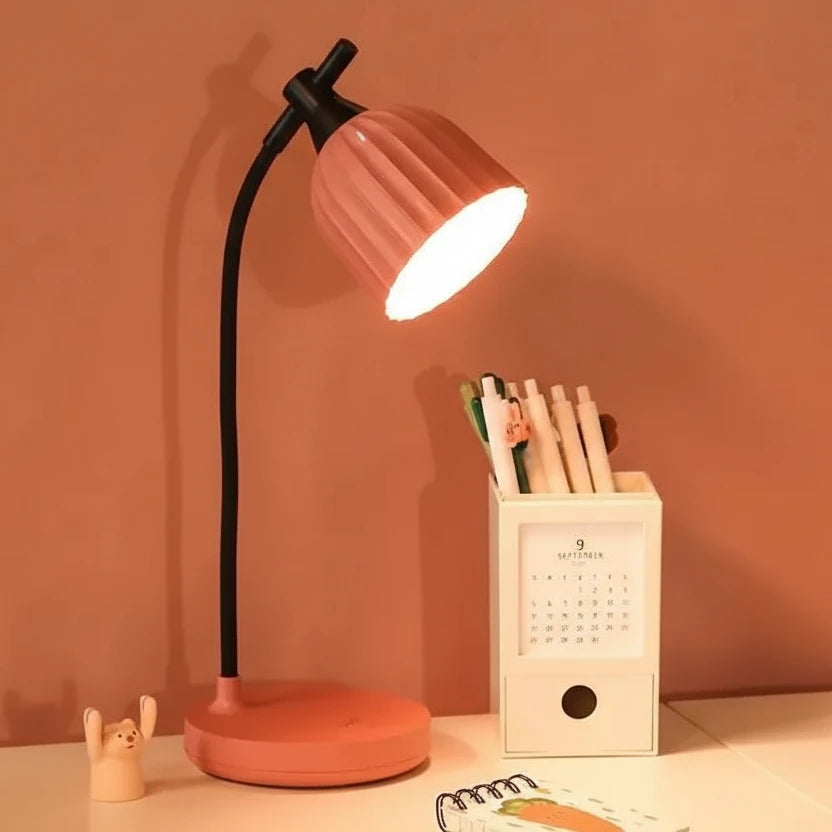 Pink desk lamp on a table with stationery items against a warm-toned wall.