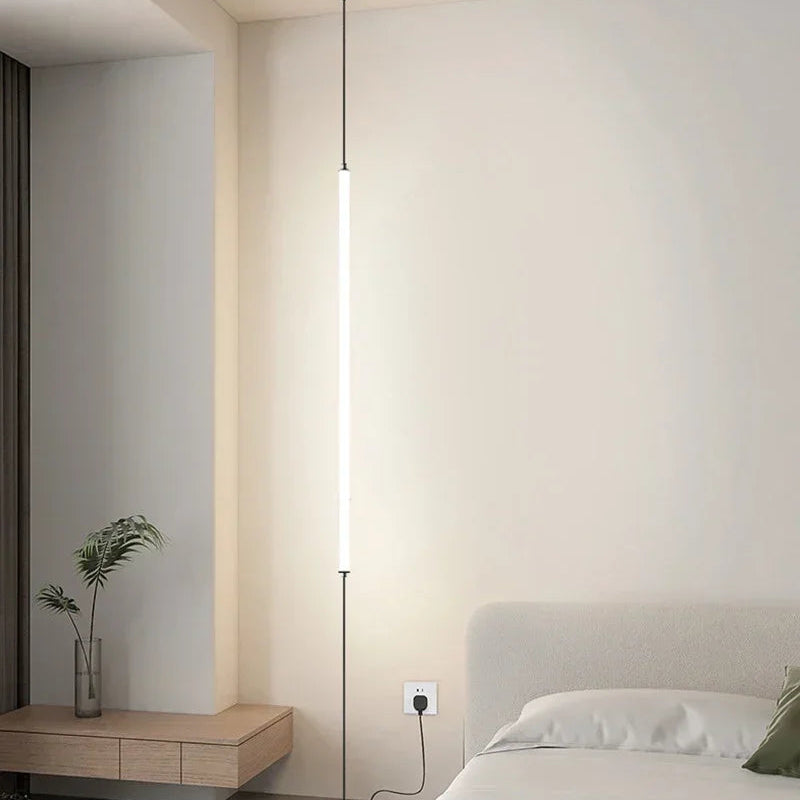 Slim floor-to-ceiling LED lamp beside a modern bedroom setting