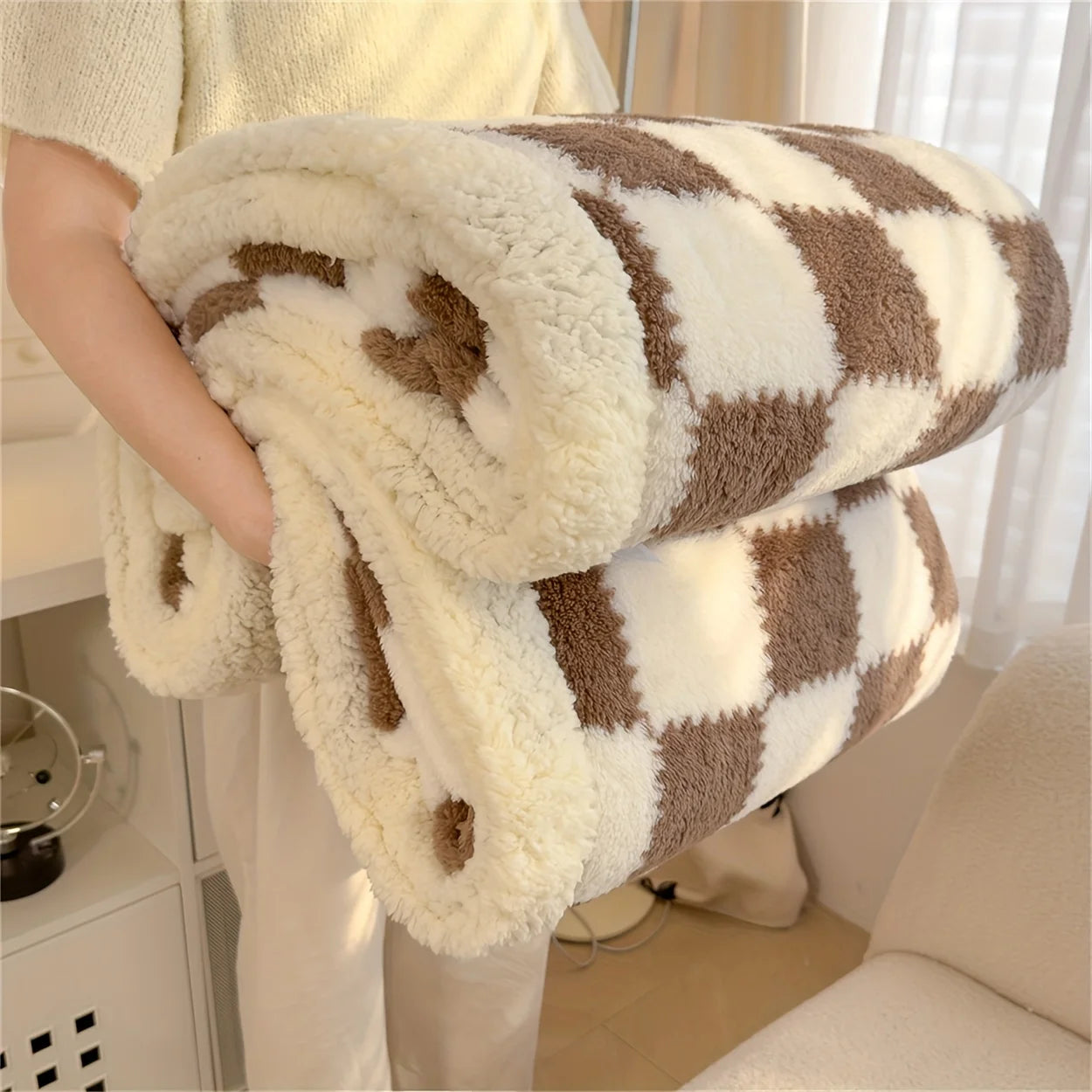 Person holding a checkered blanket with brown and white pattern in a home setting.