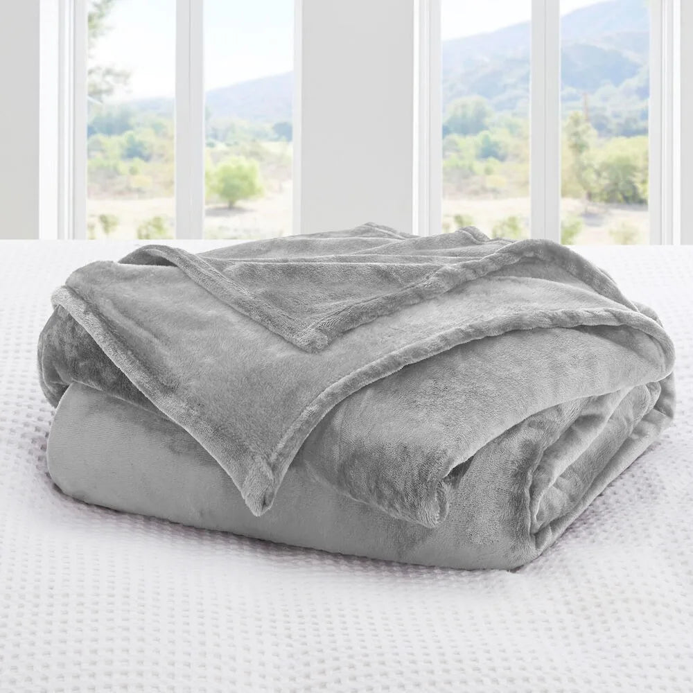 A silver grey blanket on a bed with a window view of trees and mountains