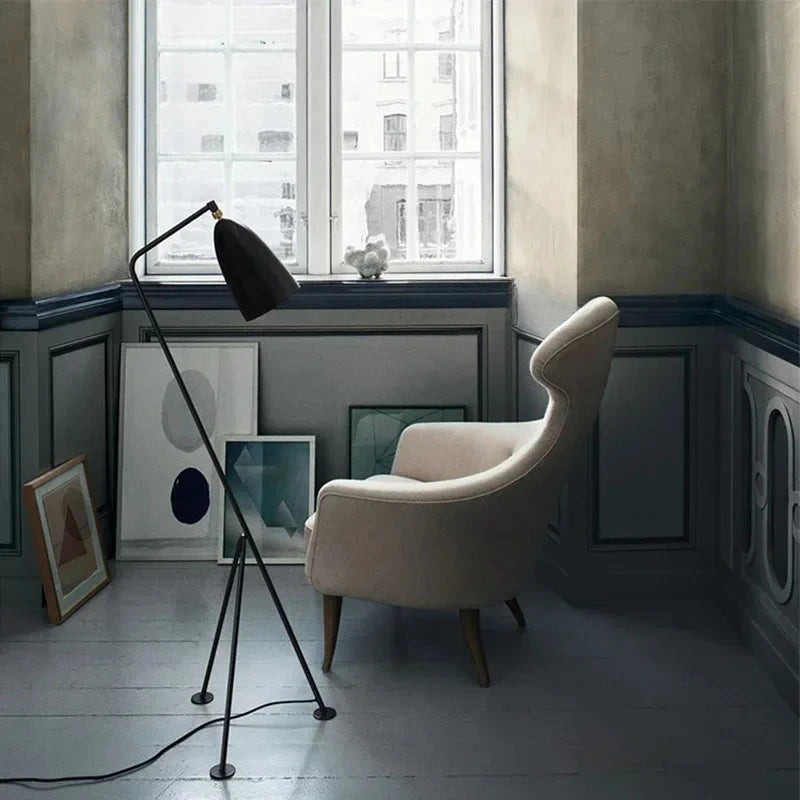 Modern room with a beige armchair, black floor lamp, and framed artwork on a light-coloured floor.