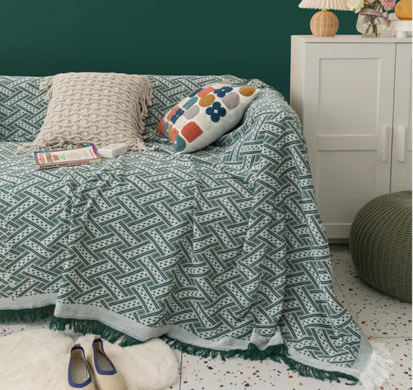 Patterned green blanket draped over a sofa with cushions and a lamp in the background.