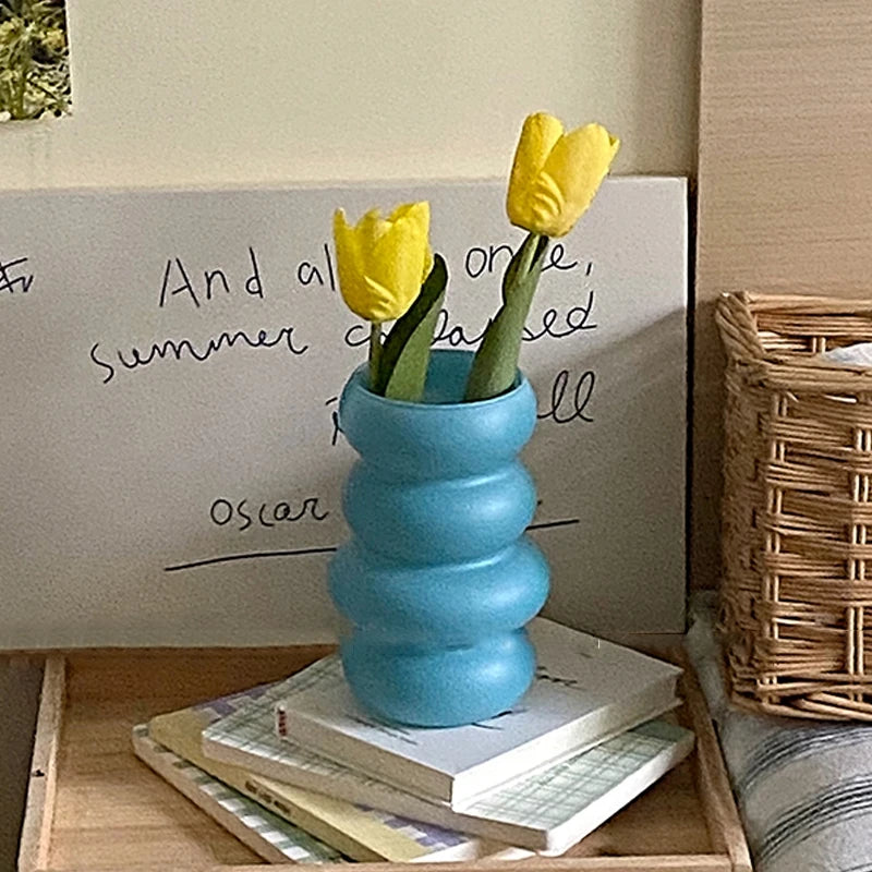 Blue vase with yellow tulips on a stack of books against a whiteboard.