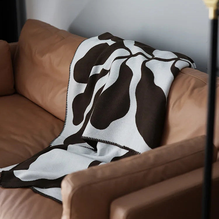 Mocha and grey abstract jacquard blanket draped over a wooden chair on a textured cream rug