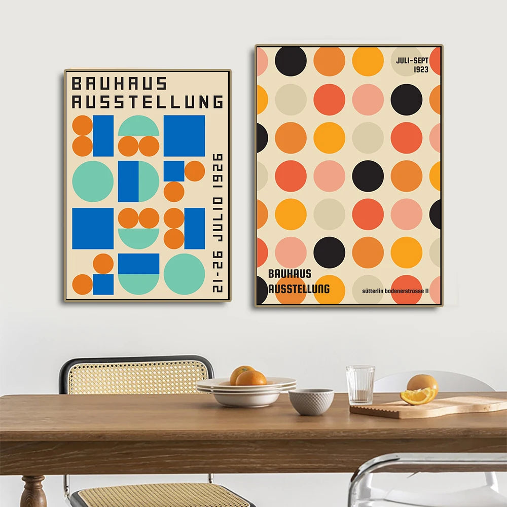 Two Bauhaus posters on a wall above a dining table with fruit and a glass.