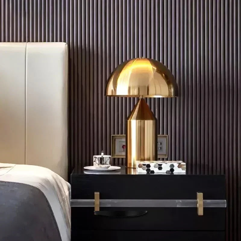 Gold table lamp on a nightstand next to a bed with a dark wall background