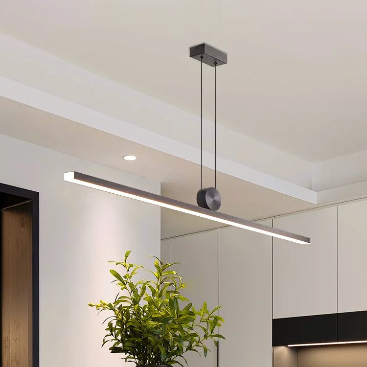 Modern pendant light fixture hanging above a table with a vase and fruits in a minimalistic room.