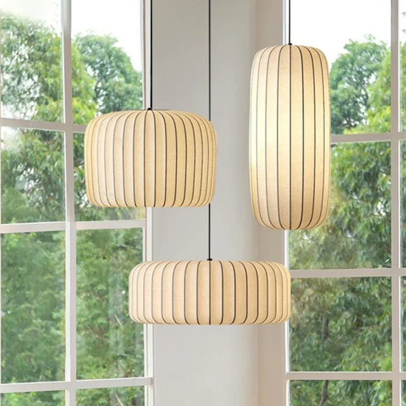 Three cylindrical pendant lights hanging in front of a window with greenery outside.