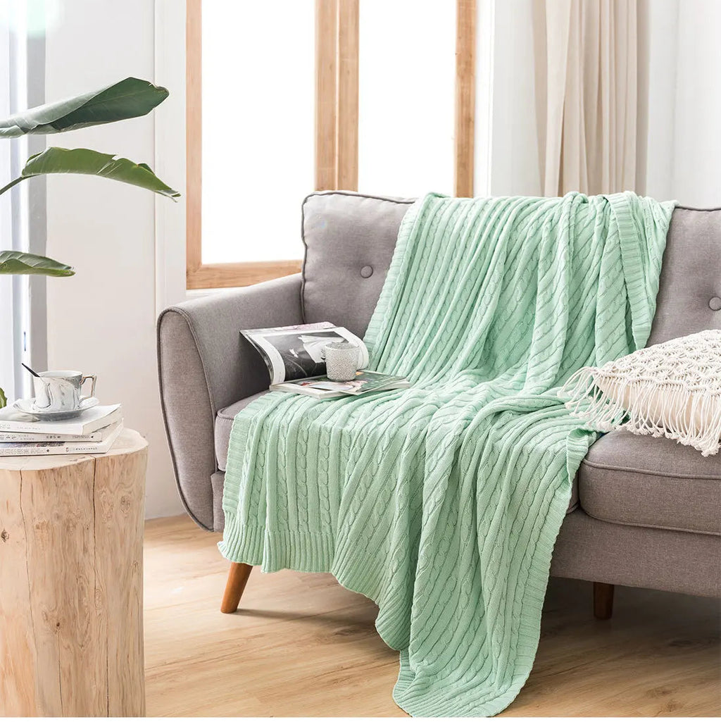Green blanket draped over a gray sofa in a living room with a plant and wooden table.
