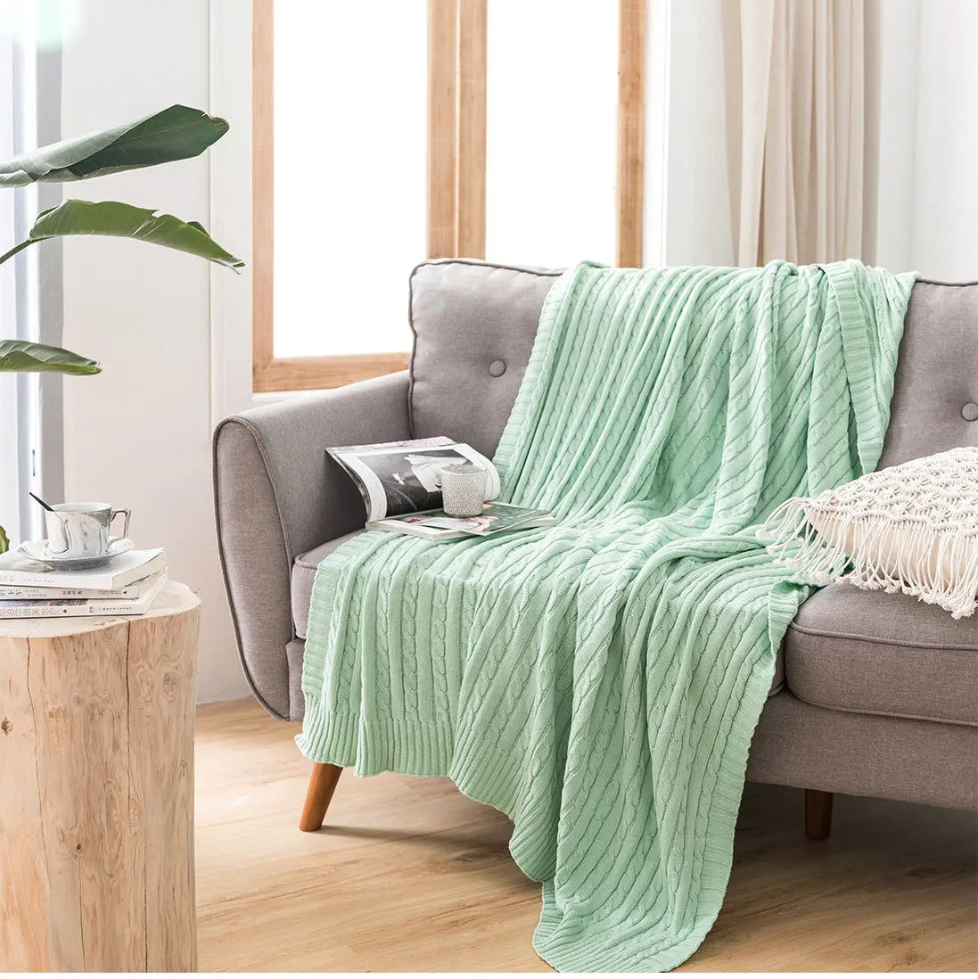 Green blanket draped over a gray sofa in a living room with a plant and wooden table.