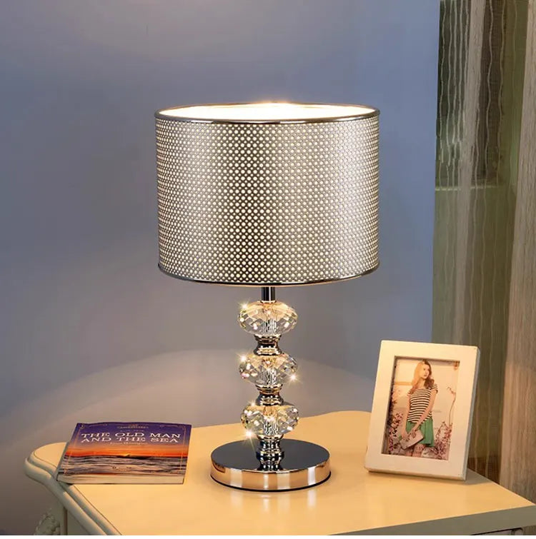 table lamp with a solid black cylindrical shade and a triple-stacked crystal base on a nightstand.