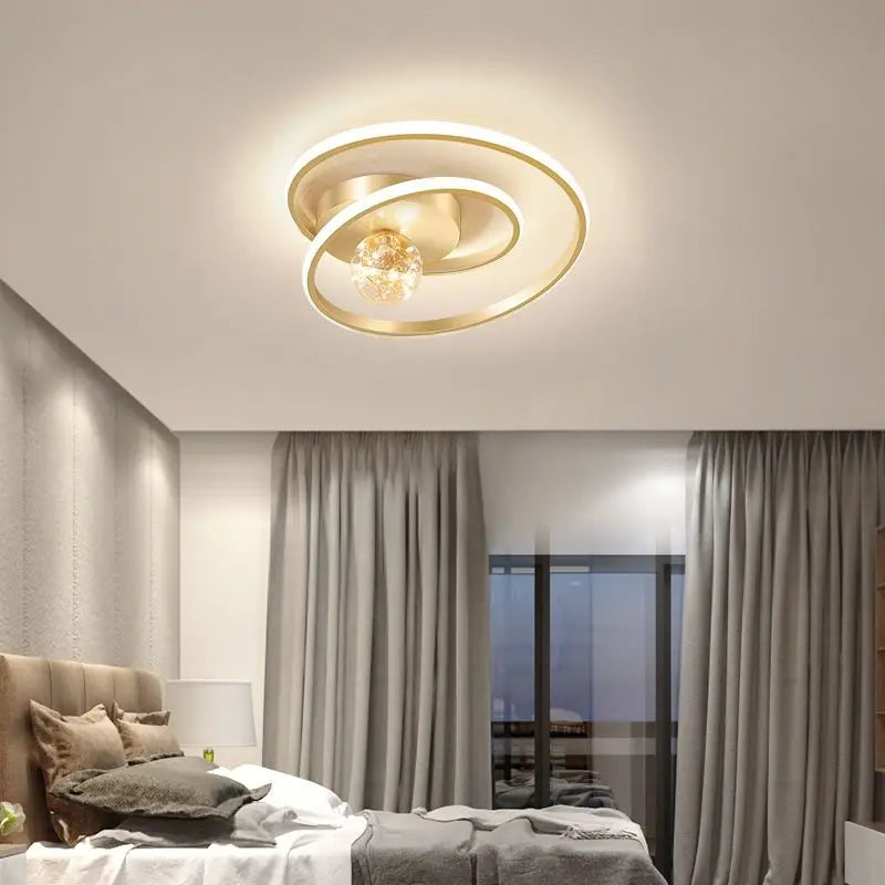 Gold Nordic spiral ceiling light with amber glass globe installed above a modern bedroom with warm ambient lighting