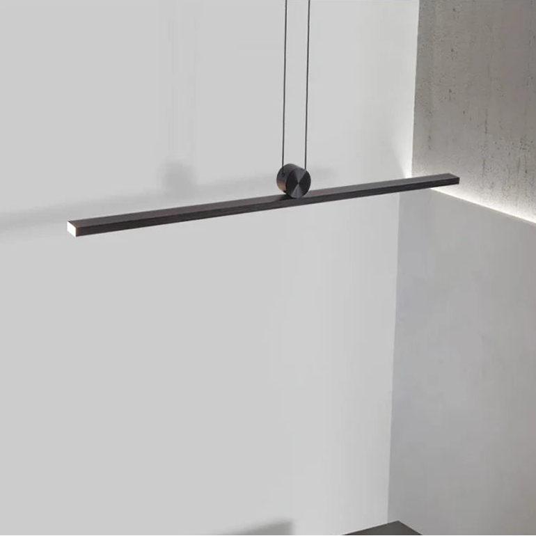 Modern black pendant light fixture on a white wall above a dark table.