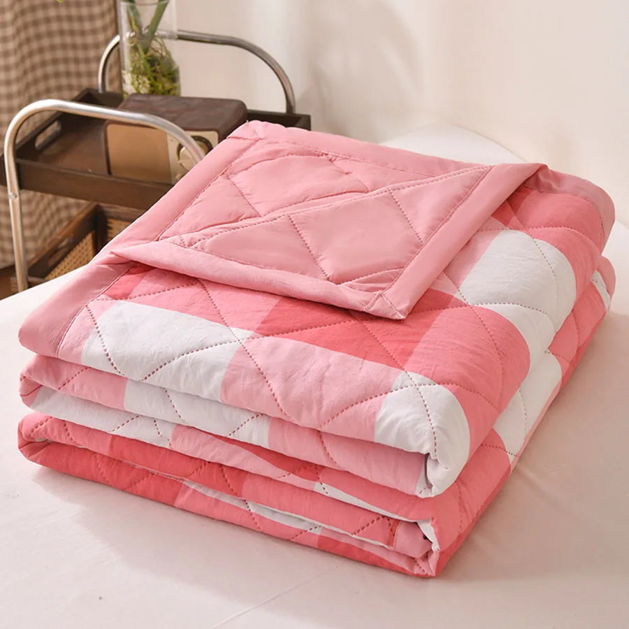Pink and white large check quilted comforter folded on a bed with a pink border