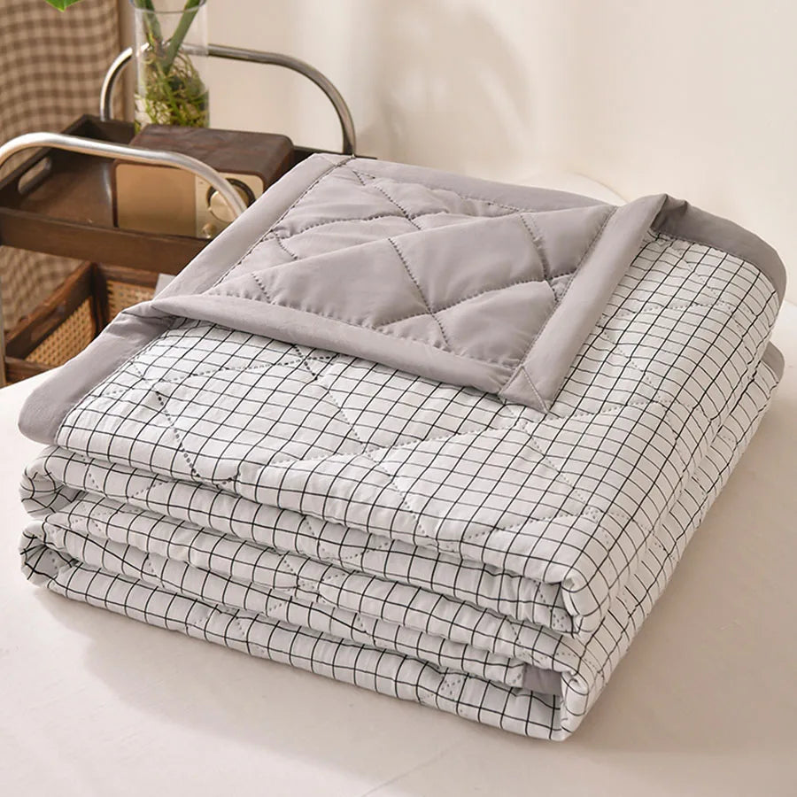 White quilted comforter with a fine black grid print and grey border, folded on a bed