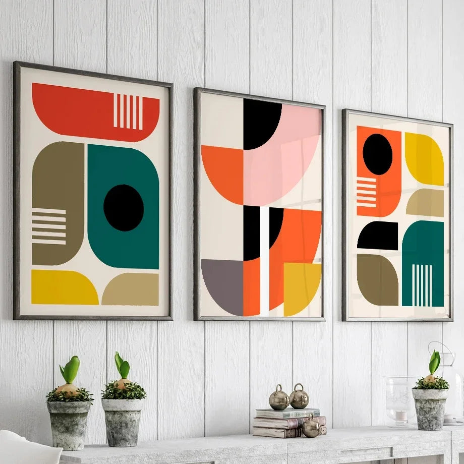Three abstract art prints on a wall with decorative items below.