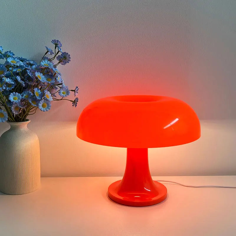 Orange mushroom shape table lamp on a surface with a vase of flowers next to it