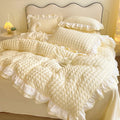 Cream-colored ruffled duvet cover set on a bed with pillows.