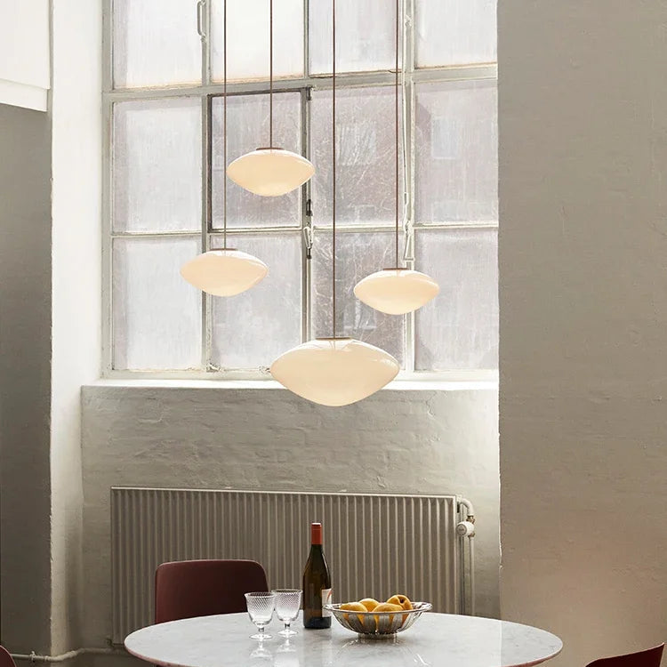 Modern dining area with round table, chairs, and pendant lights in a room with large windows.