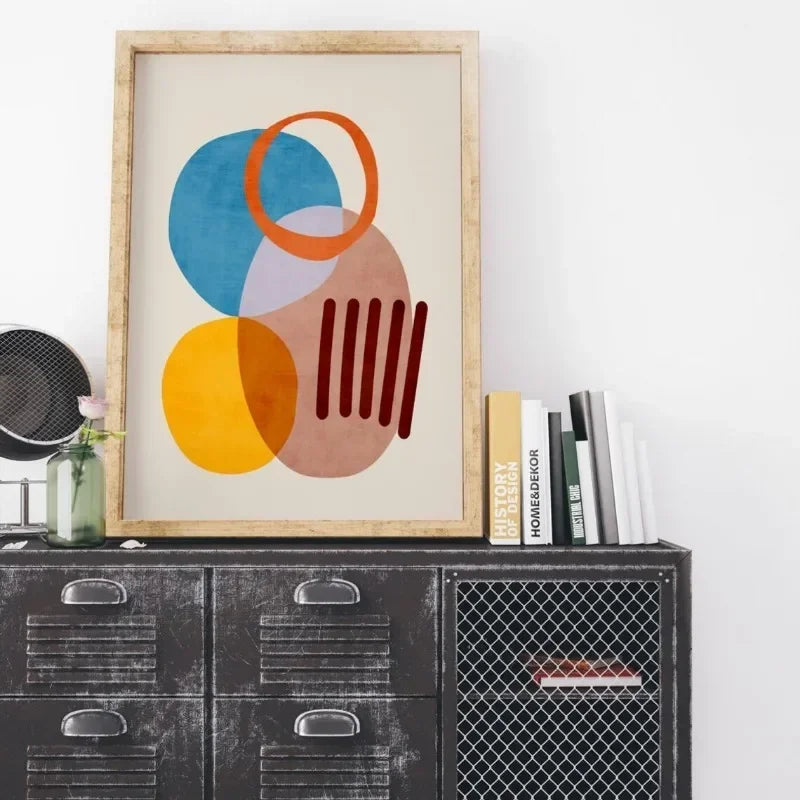 Framed abstract art piece on a shelf with books and decor items.