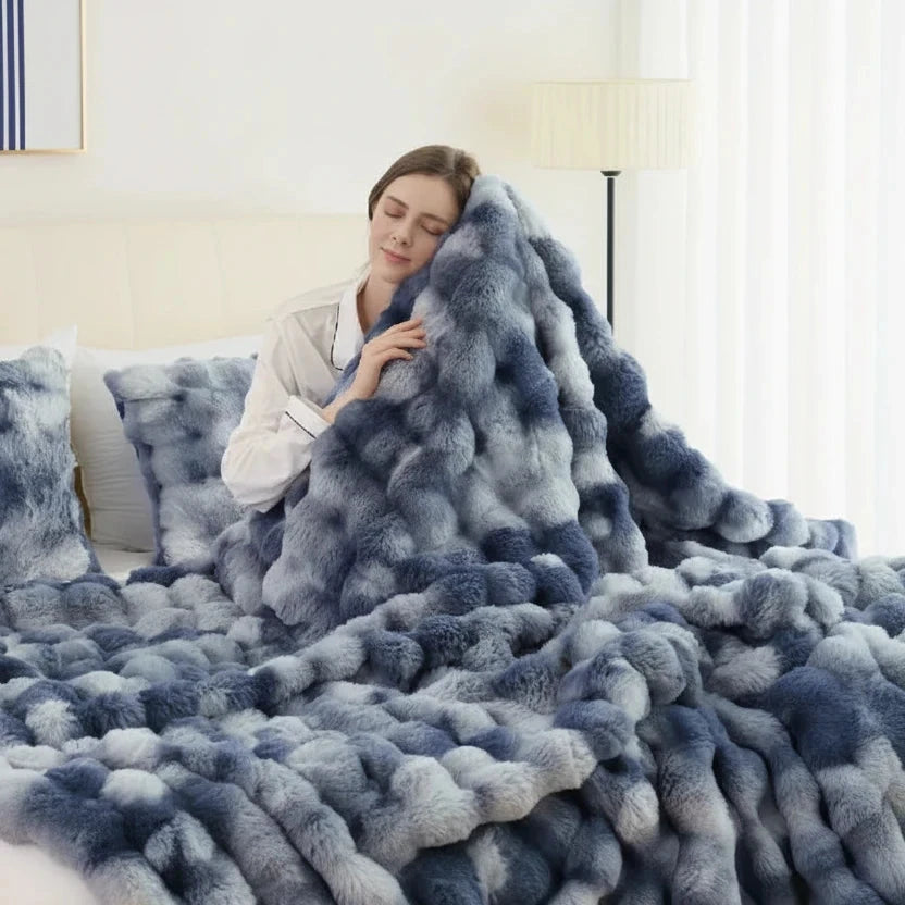 Woman wrapped in a fluffy blue blanket on a couch in a bright room.