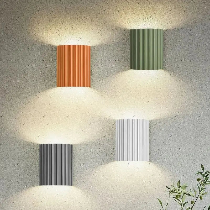 Three wall-mounted lamps with different coloured cylindrical shades on a textured wall.