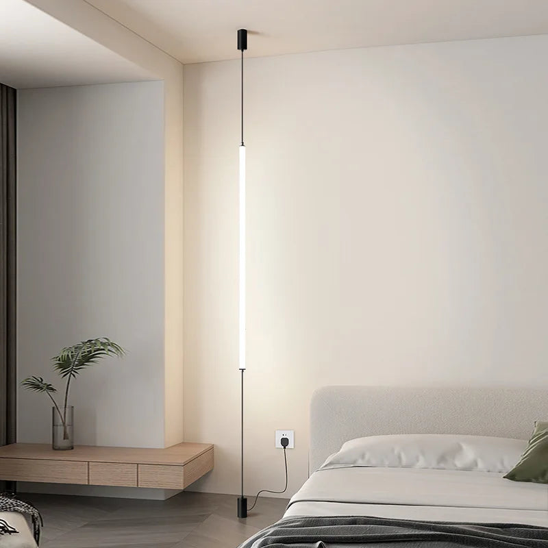 Slim floor-to-ceiling LED lamp beside a modern bedroom setting