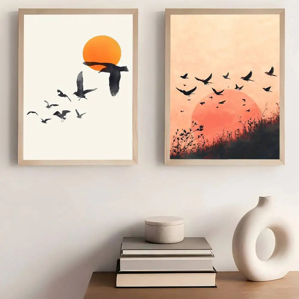 Two framed artworks of birds flying against a sunset sky, displayed on a wall above books and a vase.