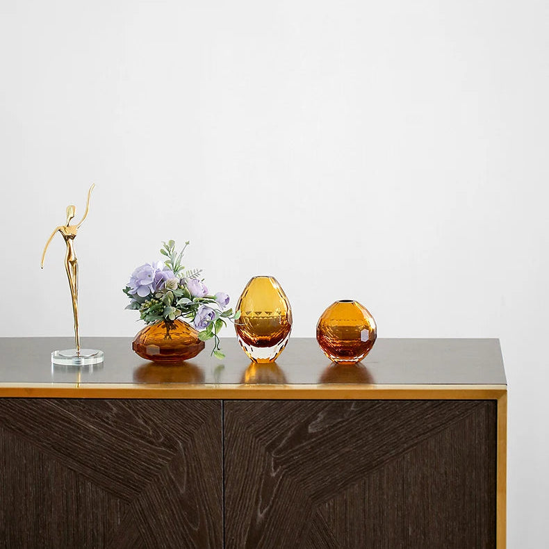 Three amber-coloured glass vases on a wooden surface with a plain background