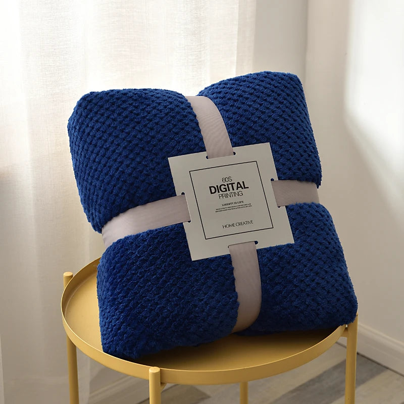 Navy blue textured blanket with a tag on a yellow round table against a white curtain background