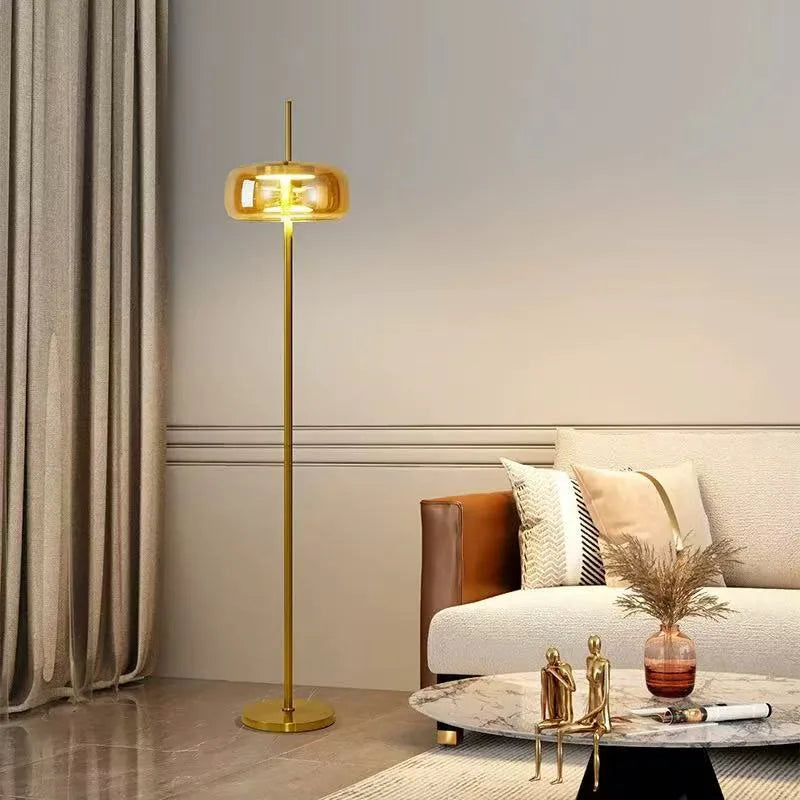 Minimalist gold floor lamp with amber glass shade lit in a warm glow.