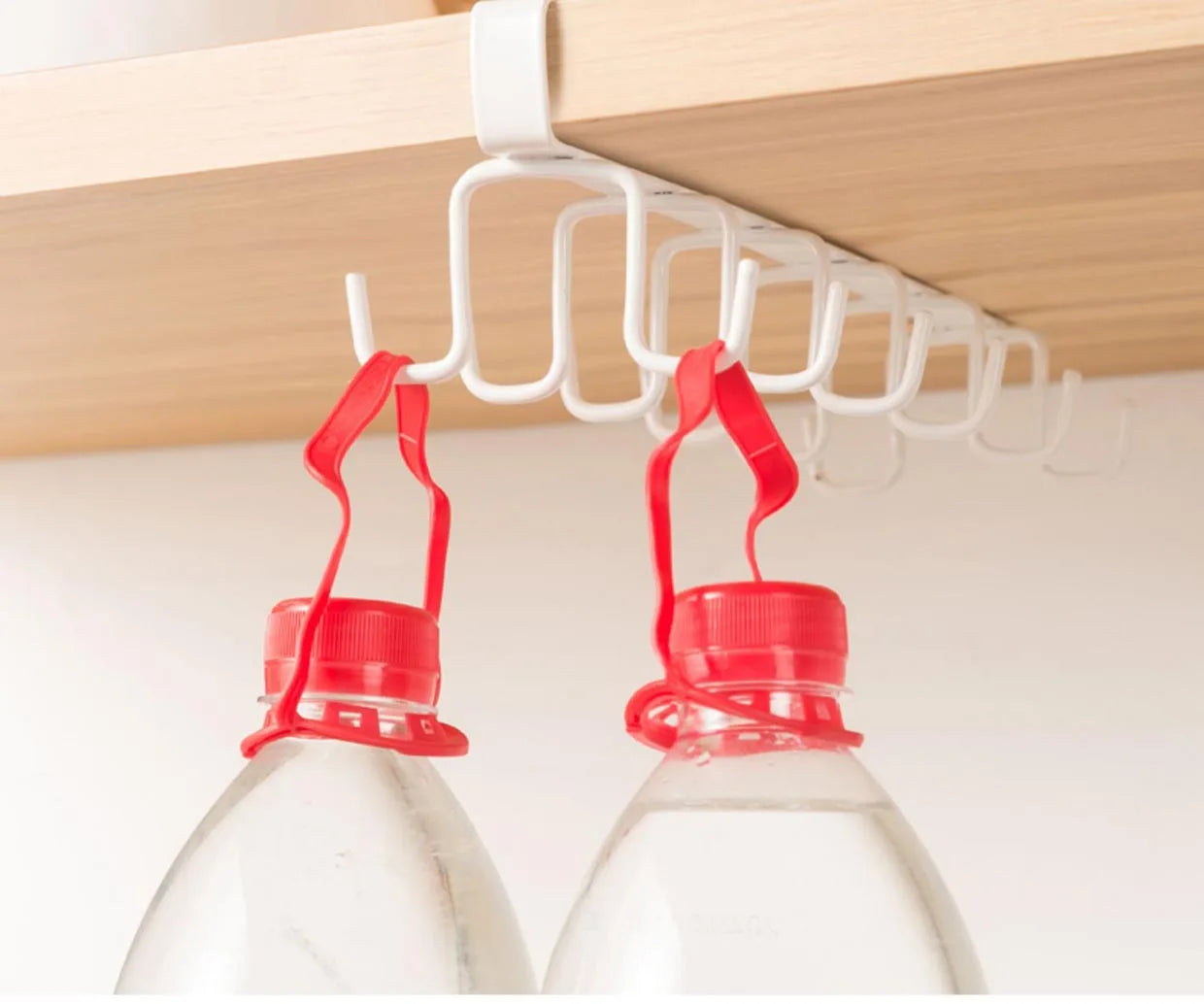 Two bottles with red caps hanging from a white hook on a kitchen cabinet shelf.