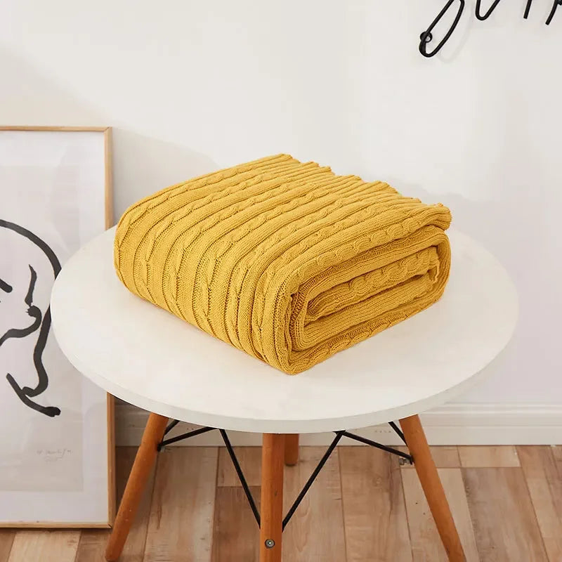 Yellow textured blanket on a white stool with a minimal background