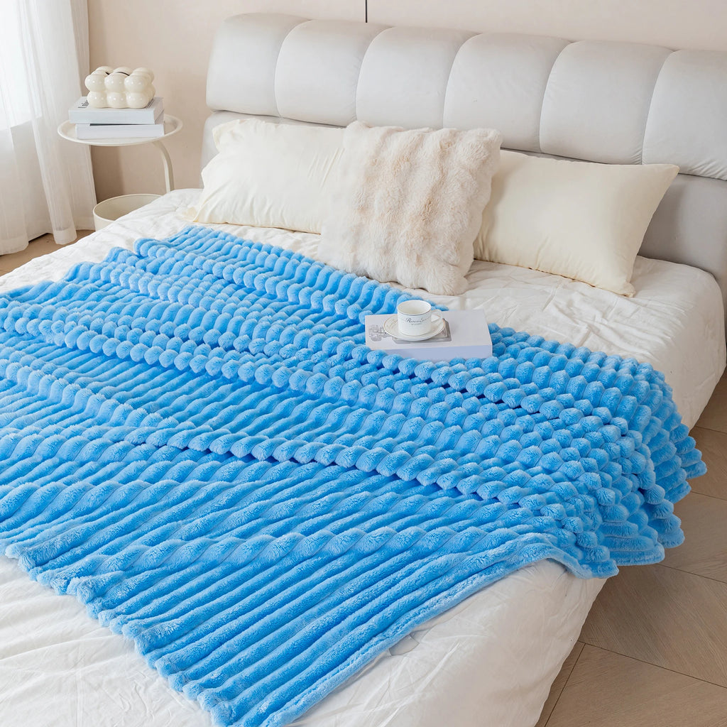 Blue textured blanket on a bed with white pillows and a light-colored headboard.