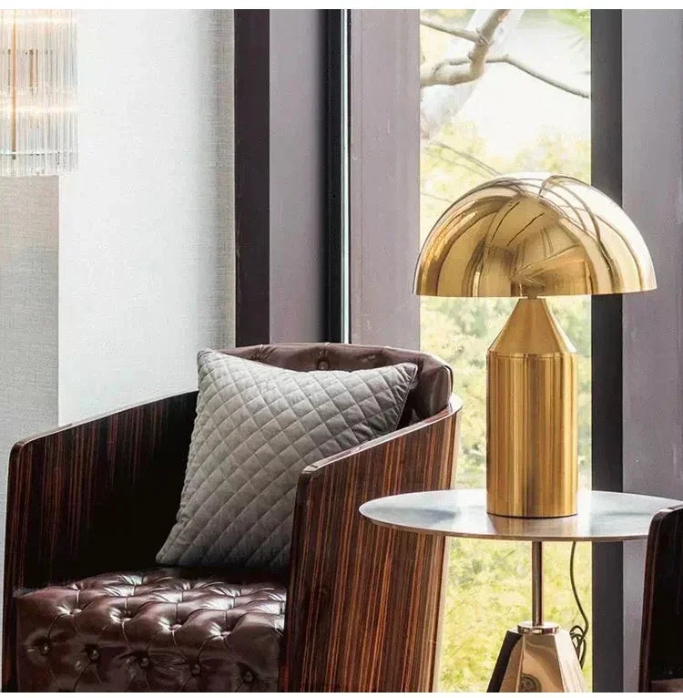 Gold table lamp on a round table next to a brown armchair with a textured cushion.