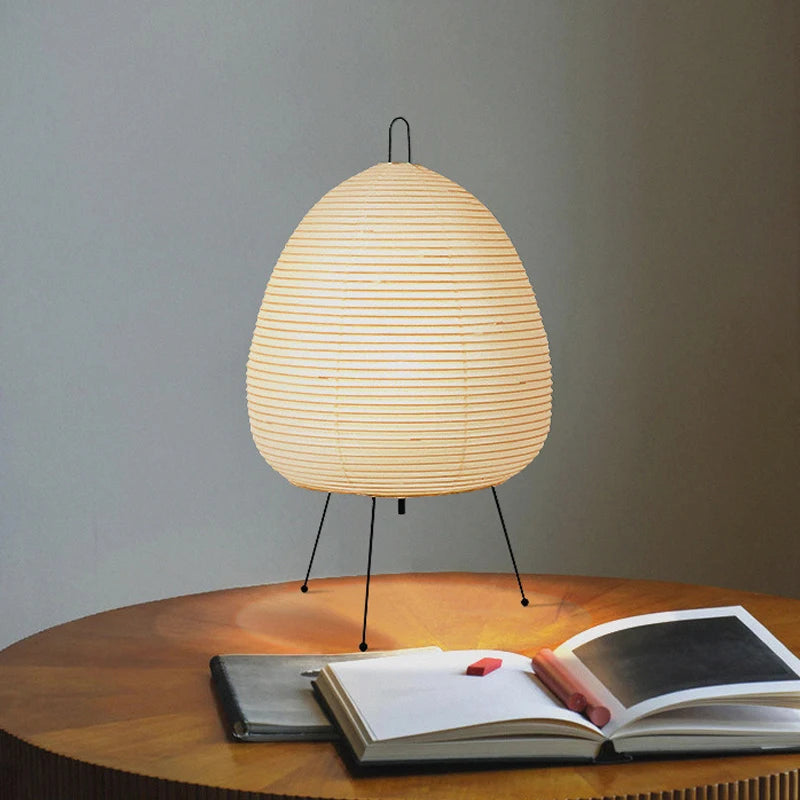 Japanese table lamp with a woven design on a wooden table next to an open book.