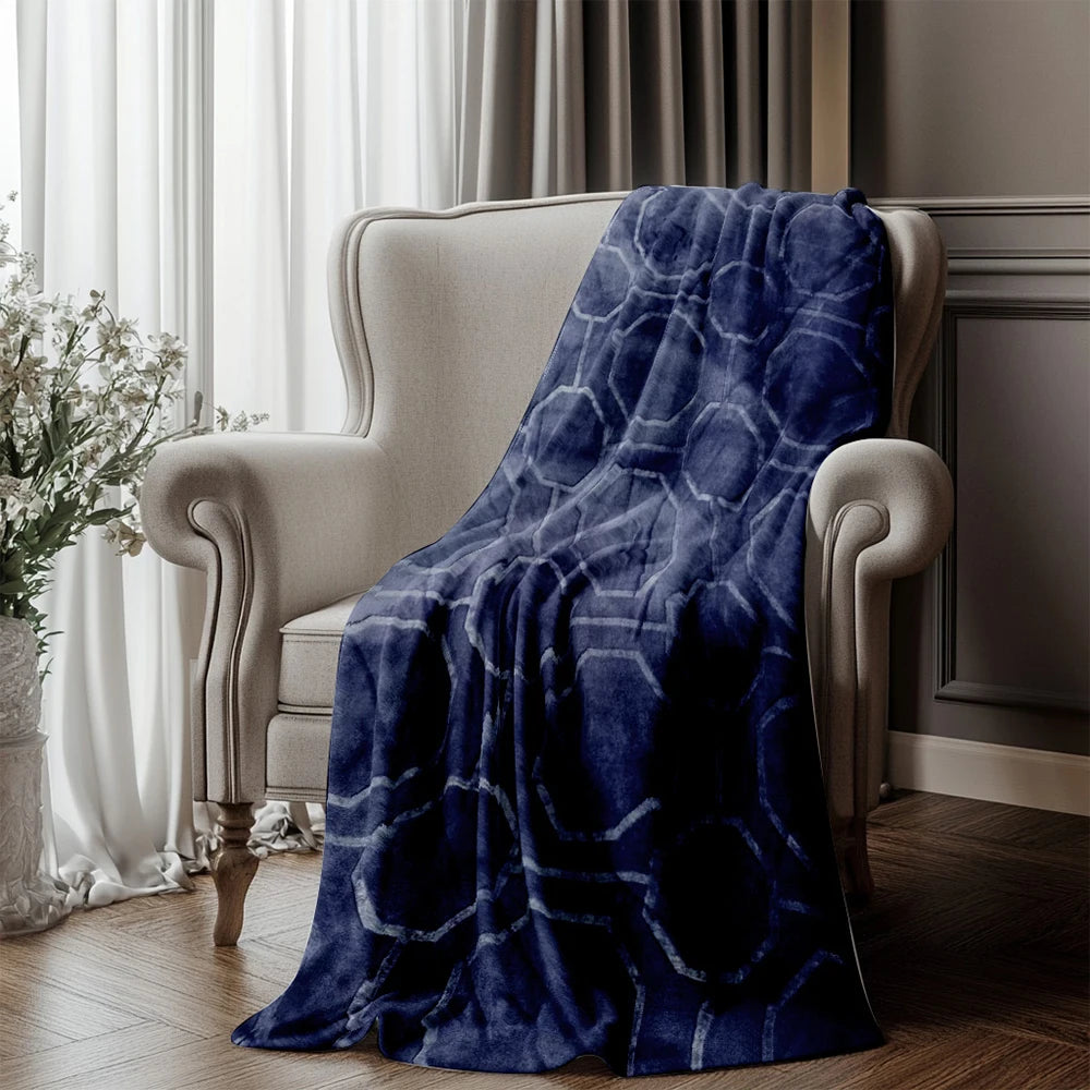 Blue patterned blanket draped over a beige armchair in a room with curtains and flowers.