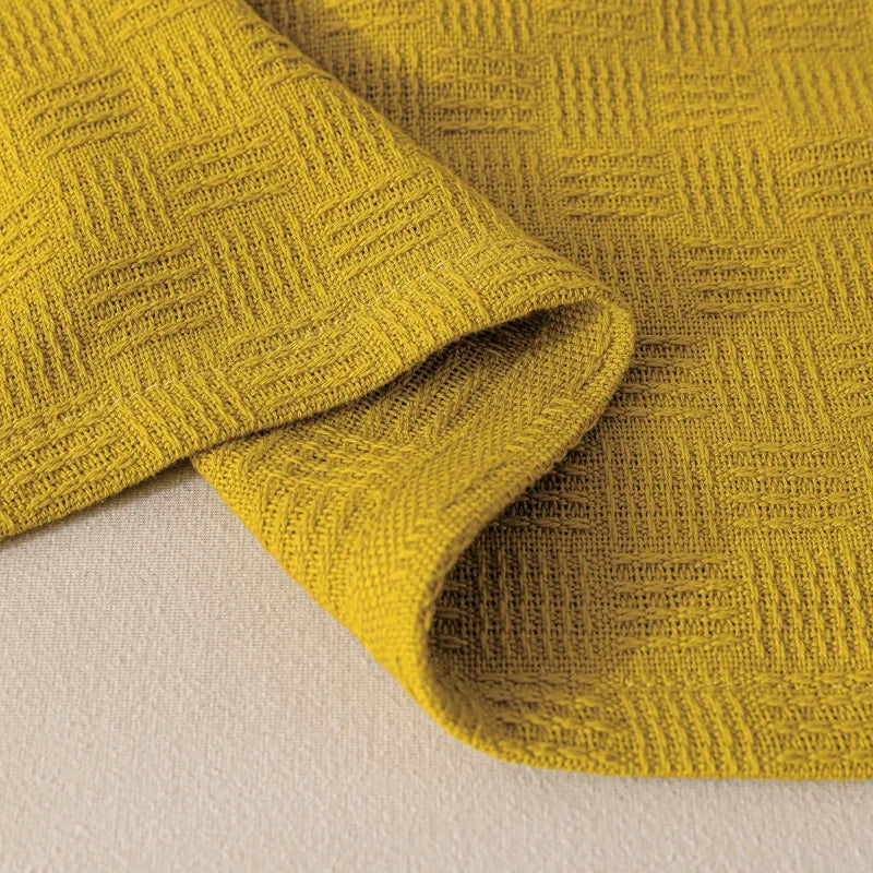 A close-up of an olive cotton knit throw blanket with textured weave pattern.