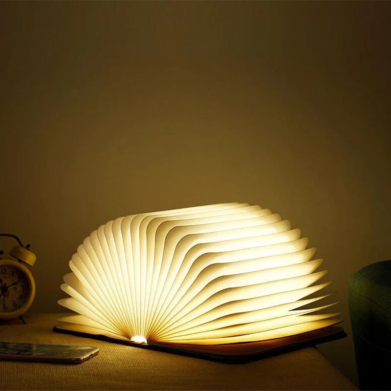 Book-shaped lamp emitting a warm glow on a wooden surface with a neutral background