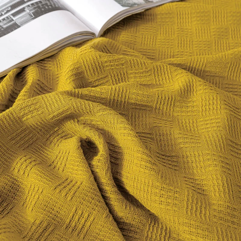 A close-up of an olive cotton knit throw blanket with textured weave pattern.