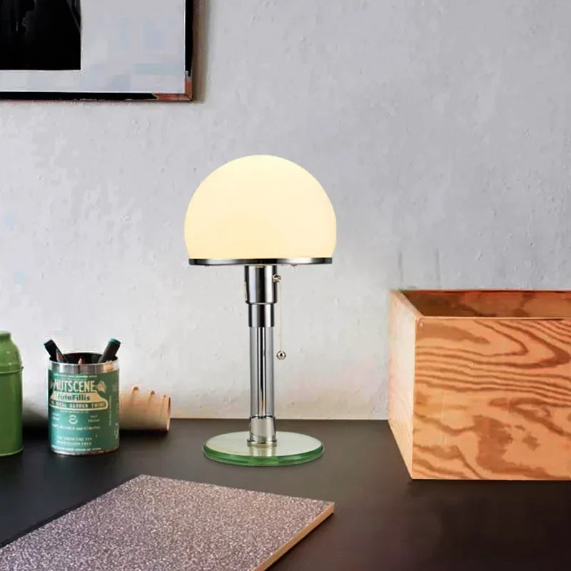 Polished chrome mushroom table lamp with a clear glass base on a dark stone surface