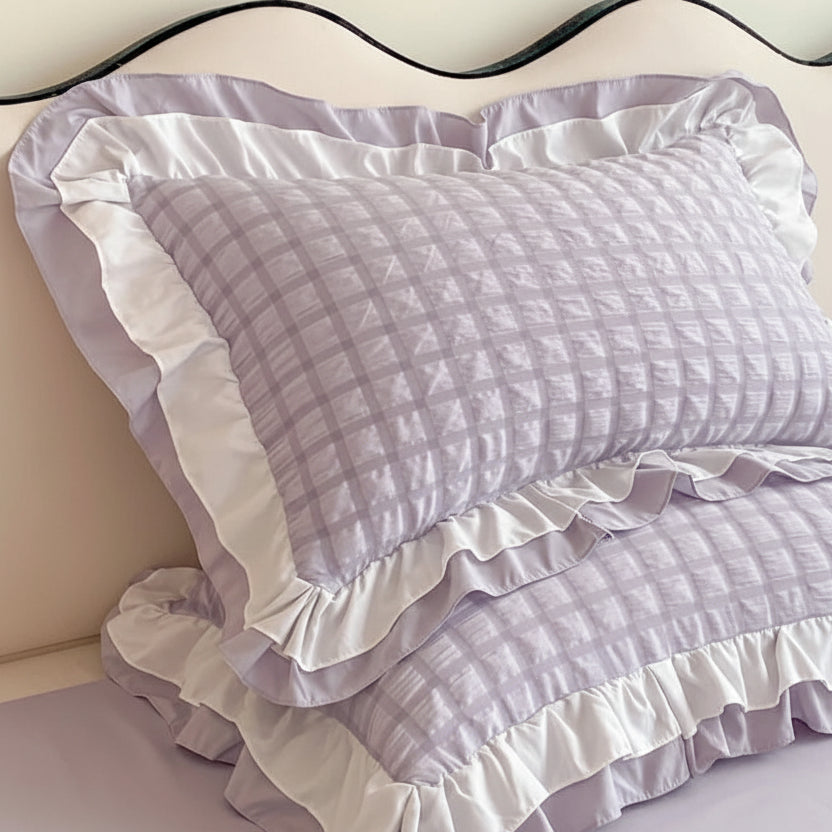 Purple and white checkered pillow with ruffle trim on a bed.