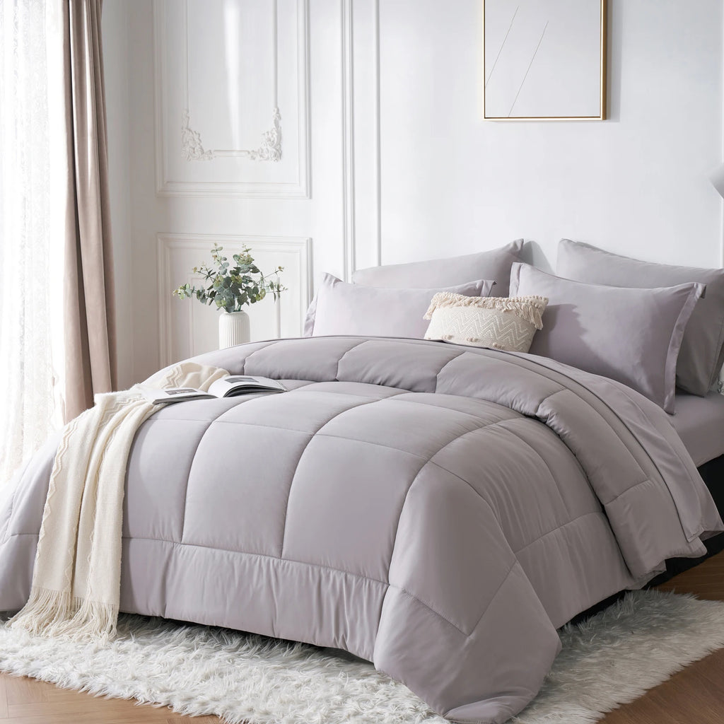 Grey comforter set on a bed in a well-lit bedroom with light decor.